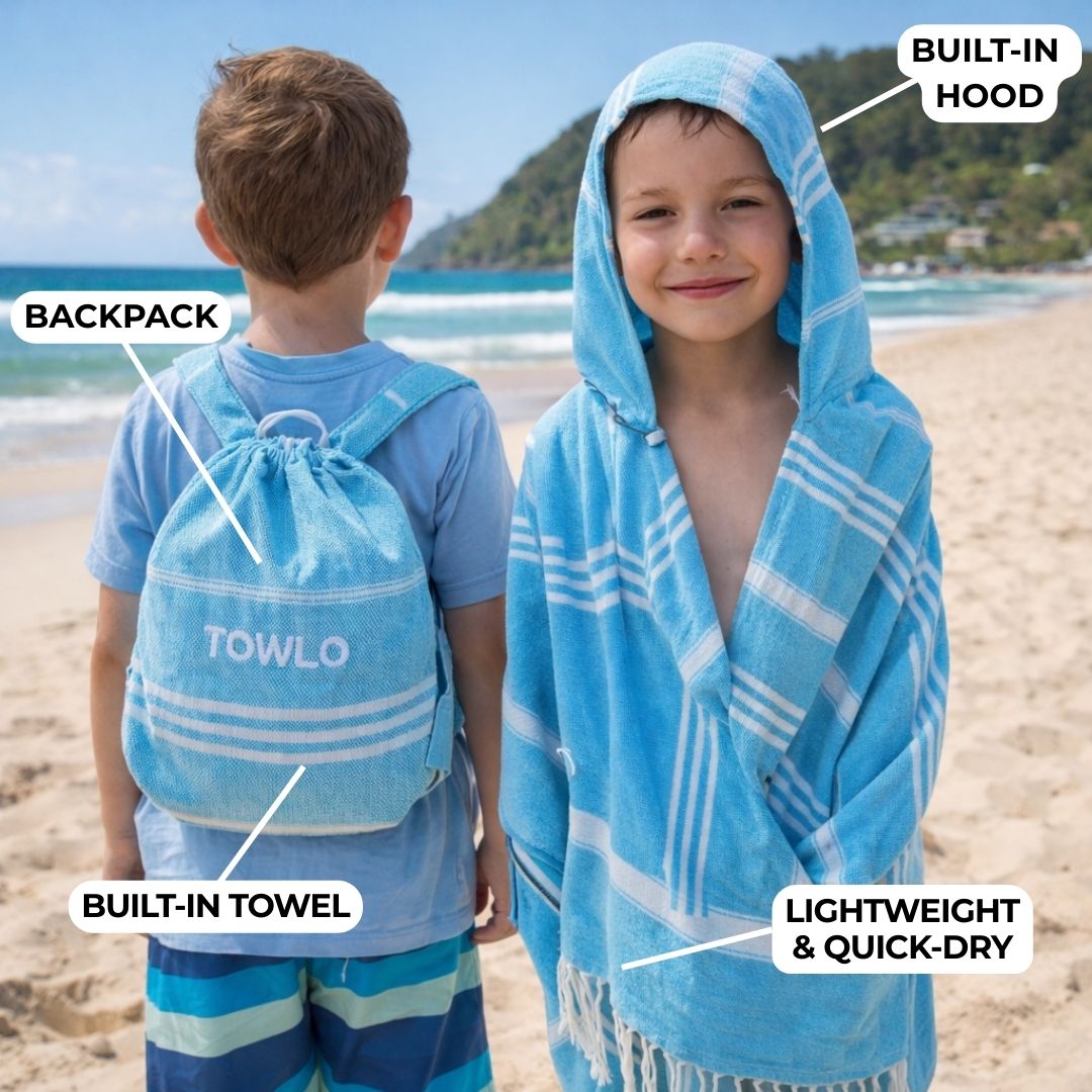 Two children on a beach with a blue towel and backpack, highlighting features like a built-in hood and towel.