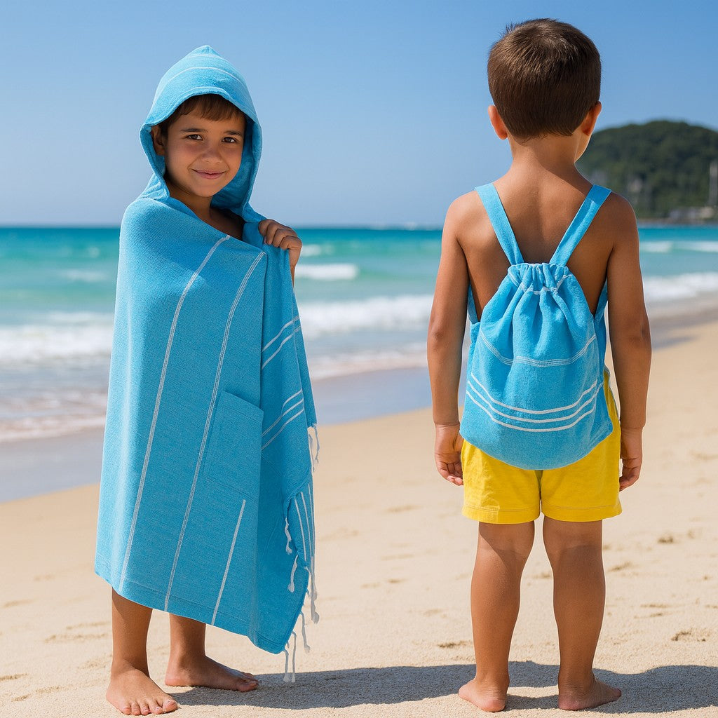 Two young boys on a sunny Gold Coast beach, one wrapped in a blue Towlo hooded towel and the other wearing a matching blue Towlo kids’ backpack towel.
