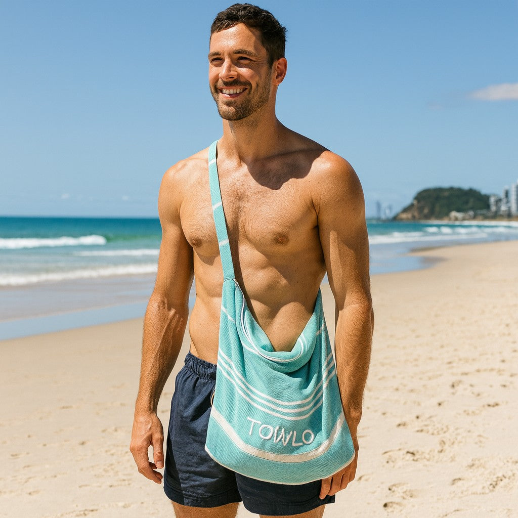 Man on a beach with a towel draped over his shoulder, featuring the 'TOWLO' brand.