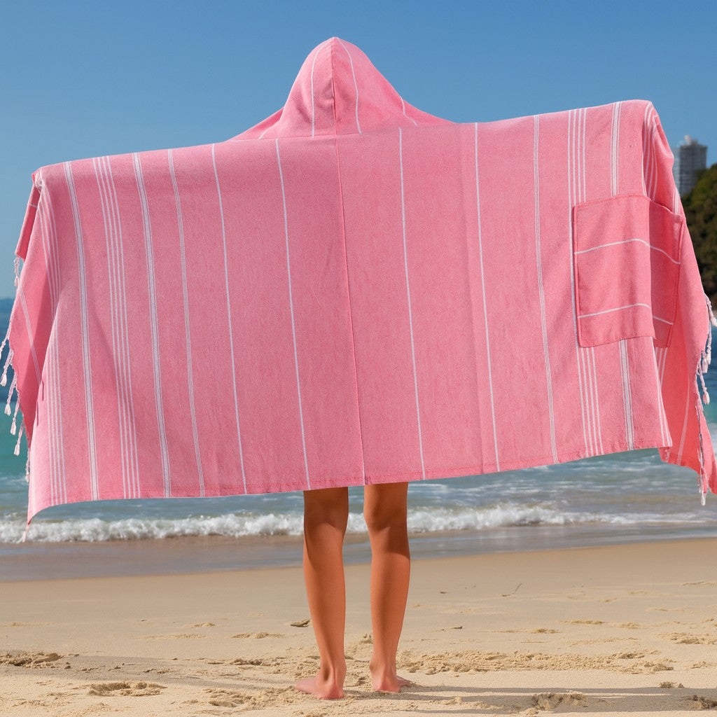 Child standing on a beach wearing a Towlo pink hooded 3-in-1 towel fully opened to show its size, stripes and built-in pocket