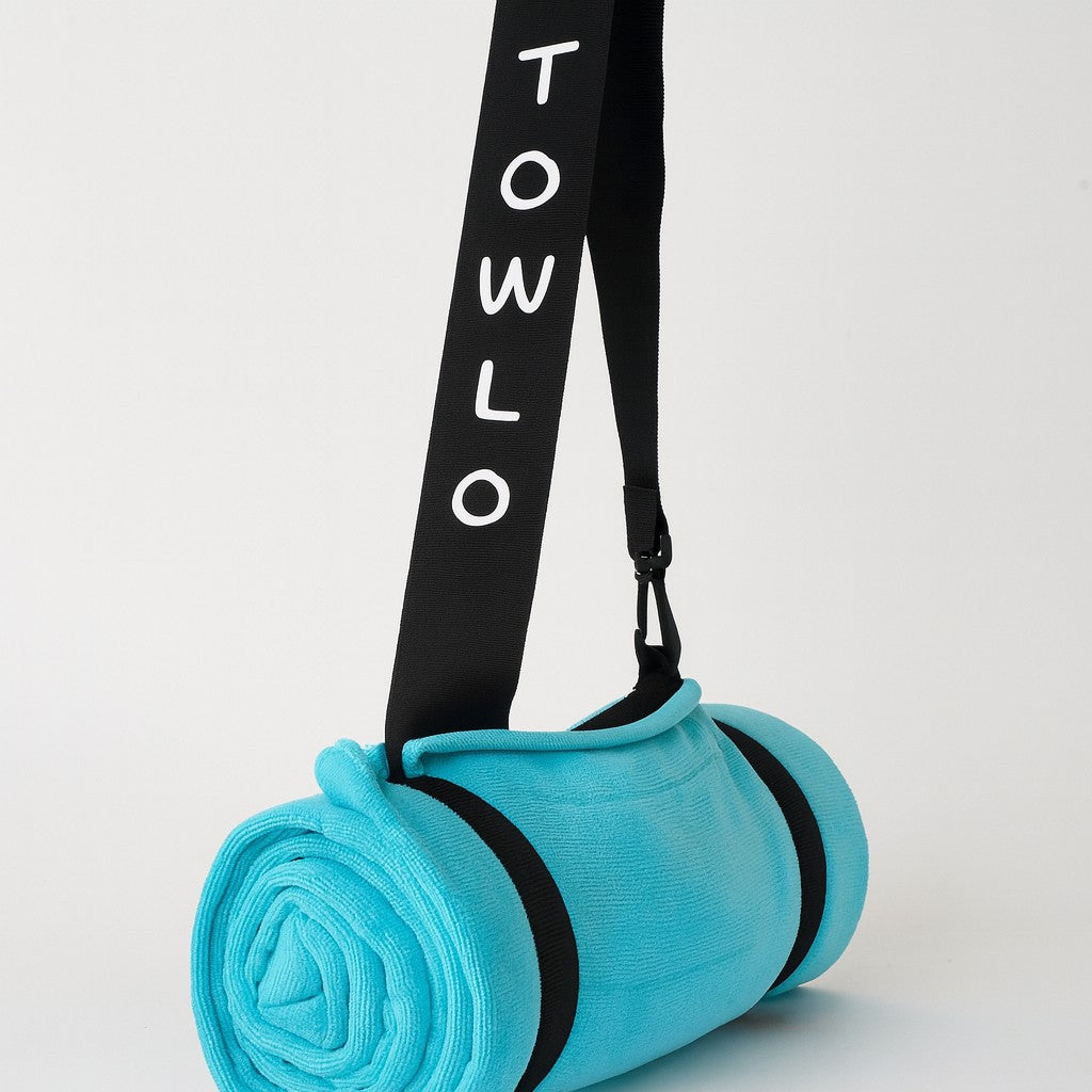 towlo aqua beach towel rolled up with black branded strap on light grey background – compact travel beach towel with built-in carry feature