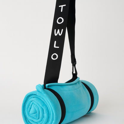 towlo aqua beach towel rolled up with black branded strap on light grey background – compact travel beach towel with built-in carry feature