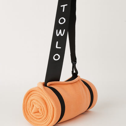 towlo peach beach towel rolled up with black shoulder strap on white background